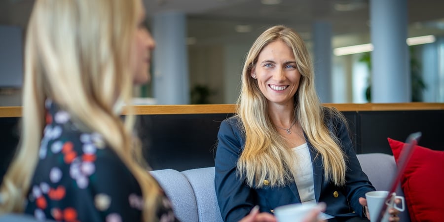 Two business women sitting on a sofa with laptops.